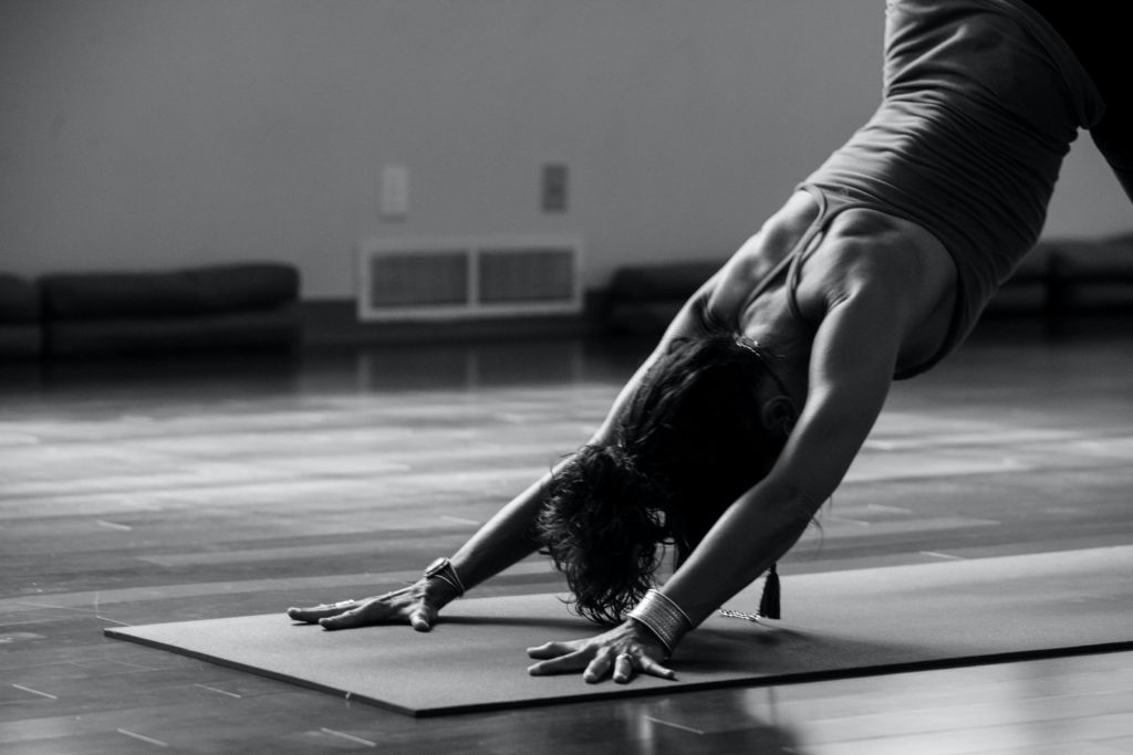 The picture depicts a woman performing a stretching exercise, bending forward with her hands resting on the ground